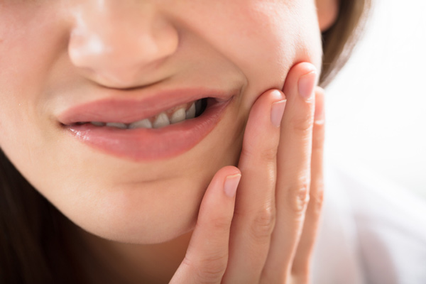 A woman with gum disease holding her cheeck at Encinitas Periodontics & Dental Implants in Encinitas, CA